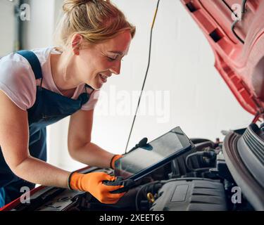 Mécanicien automobile féminin avec tablette numérique regardant sous le capot des diagnostics de voiture en cours d'exécution Banque D'Images