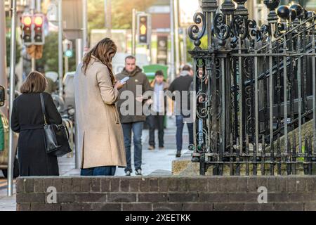 La vie quotidienne. Jeune femme stylée dans la ville avec son téléphone portable tout en marchant dans une rue de la ville. Dublin, Irlande. Banque D'Images