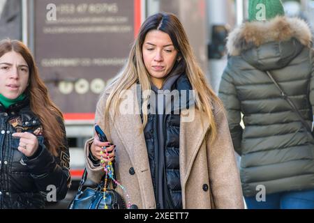 La vie quotidienne. Jeune femme stylée dans la ville avec son téléphone portable tout en marchant dans une rue de la ville. Dublin, Irlande. Banque D'Images