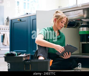 Plombier femelle avec tablette numérique fixant l'unité d'élimination des déchets dans l'évier de cuisine domestique Banque D'Images