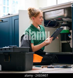 Plombier femelle avec tablette numérique fixant l'unité d'élimination des déchets dans l'évier de cuisine domestique Banque D'Images