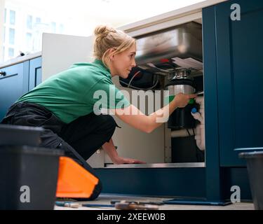 Plombier femelle avec tablette numérique fixant l'unité d'élimination des déchets dans l'évier de cuisine domestique Banque D'Images