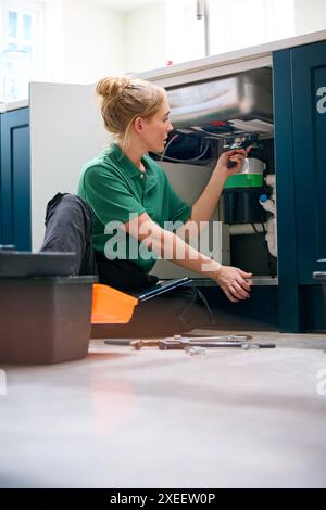 Plombier femelle avec tablette numérique fixant l'unité d'élimination des déchets dans l'évier de cuisine domestique Banque D'Images