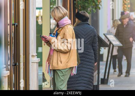 Portrait de rue d'une jeune femme restant devant une porte fermée avec son téléphone portable et son café, Dublin, Irlande. Banque D'Images