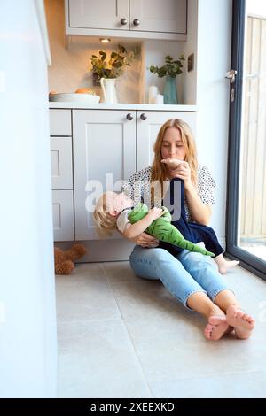 Mère aimante jouant au jeu avec le jeune fils et les jouets assis sur le sol à la maison dans la cuisine ensemble Banque D'Images