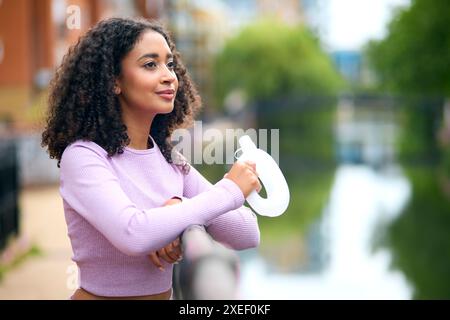 Femme portant des vêtements de fitness eau potable pendant l'exercice courir le long du chemin par la rivière dans la zone urbaine Banque D'Images