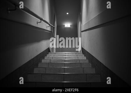 Marches menant vers le haut et une lumière au bout du couloir avec un panneau de sortie lumineux. Un couloir avec des marches, éclairé par des lampes, balustrade, porte à l'en Banque D'Images