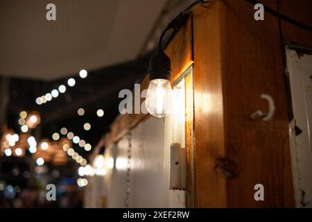 Une ampoule incandescente est suspendue au-dessus de la porte dans le coin de la pièce sur un fil et brille brillamment. Il y a des guirlandes floues de lampes dans la forme Banque D'Images