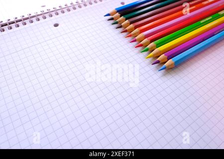 fond d'école, crayons de couleur reposent sur une feuille de papier, un cahier ouvert sur une spirale, un bloc de collège dans une cage, gros plan, le concept d'étudiant Banque D'Images