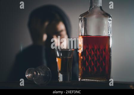 Portrait de solitaire, déprimé, jeune homme malheureusement assis avec une bouteille de whisky. Banque D'Images