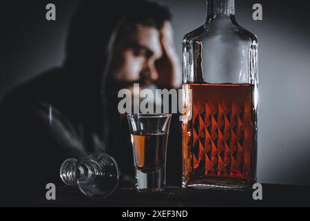 Portrait de solitaire, déprimé, jeune homme malheureusement assis avec une bouteille de whisky. Banque D'Images