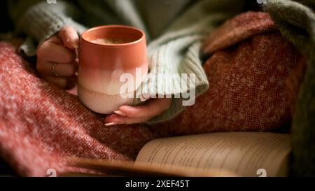 Gros plan de femme à la maison en hiver Jumper avec boisson chaude réchauffante de café dans le livre de lecture de tasse Banque D'Images