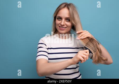 Charmante femme blonde européenne peignant ses cheveux sur un fond isolé bleu Banque D'Images