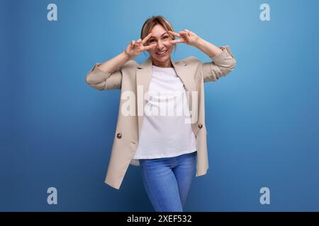 Gros plan d'une jeune femme blonde de type positif dans une veste beige avec des émotions sur son visage dans le studio Banque D'Images