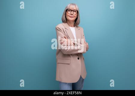 Une femme mature avec les cheveux gris dans une veste se tient en toute confiance sur un fond lumineux avec un espace de copie Banque D'Images
