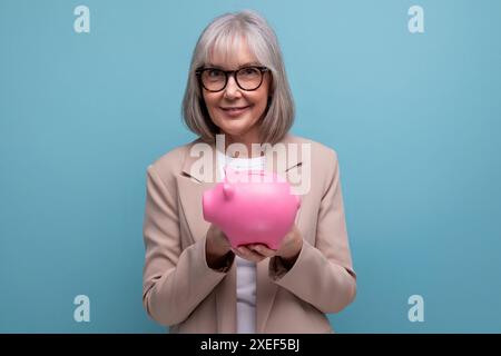 Mignonne vieille femme dans une veste avec une tirelire d'épargne d'argent sur un fond lumineux avec espace de copie Banque D'Images