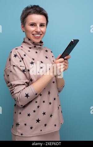 Jeune jolie femme avec des caractéristiques enfantines avec une coupe de cheveux courte habillée dans un costume beige chattant en utilisant une connexion en ligne et un Banque D'Images