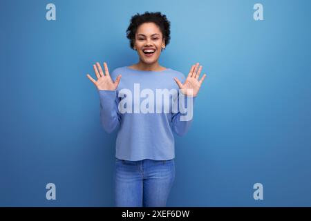Heureuse jeune femme latine des années 20 avec les cheveux noirs dans un chignon sur fond bleu Banque D'Images