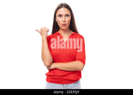 Portrait d'une jolie jeune brune européenne dans un t-shirt rouge faisant activement des gestes avec son index vers le mur Banque D'Images