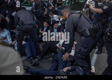 Beni Brak, Israël. 27 juin 2024. Les Juifs ultra orthodoxes se bagarrent avec la police anti-émeute israélienne alors qu'ils bloquent l'autoroute dans un sit-in de protestation contre le service militaire obligatoire en Israël. Les neuf juges de la Cour suprême de Jérusalem ont jugé qu'il n'y avait pas de fondement juridique pour exempter les ultra-orthodoxes du service militaire obligatoire et ont approuvé deux requêtes demandant leur conscription immédiate. Crédit : Ilia Yefimovich/dpa/Alamy Live News Banque D'Images