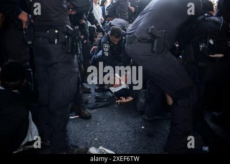 Beni Brak, Israël. 27 juin 2024. Les Juifs ultra orthodoxes se bagarrent avec la police anti-émeute israélienne alors qu'ils bloquent l'autoroute dans un sit-in de protestation contre le service militaire obligatoire en Israël. Les neuf juges de la Cour suprême de Jérusalem ont jugé qu'il n'y avait pas de fondement juridique pour exempter les ultra-orthodoxes du service militaire obligatoire et ont approuvé deux requêtes demandant leur conscription immédiate. Crédit : Ilia Yefimovich/dpa/Alamy Live News Banque D'Images