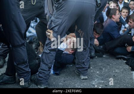 Beni Brak, Israël. 27 juin 2024. Les Juifs ultra orthodoxes se bagarrent avec la police anti-émeute israélienne alors qu'ils bloquent l'autoroute dans un sit-in de protestation contre le service militaire obligatoire en Israël. Les neuf juges de la Cour suprême de Jérusalem ont jugé qu'il n'y avait pas de fondement juridique pour exempter les ultra-orthodoxes du service militaire obligatoire et ont approuvé deux requêtes demandant leur conscription immédiate. Crédit : Ilia Yefimovich/dpa/Alamy Live News Banque D'Images