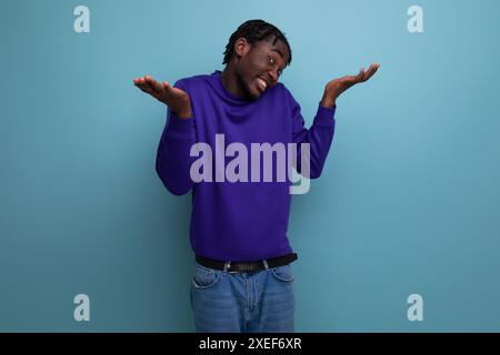 Portrait d'un jeune adulte afro-américain frustré en jeans isolé sur fond Uni Banque D'Images