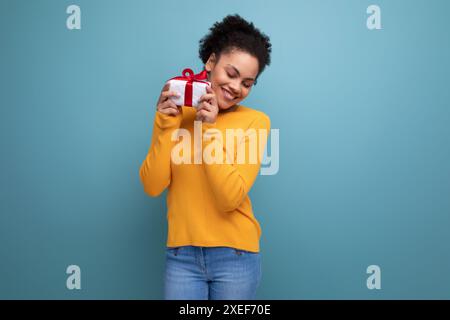 Joyeuse jeune brune latine femme adulte jeune femme adulte en pull jaune a reçu un cadeau dans une boîte Banque D'Images