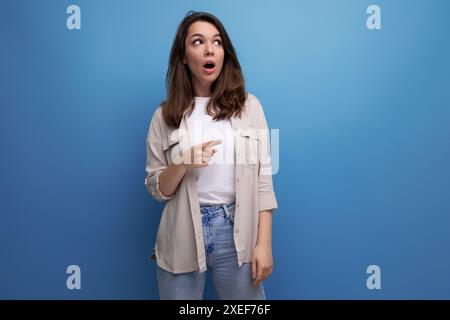 Inspiré brune intelligente jeune femme dans un look élégant possède des informations sur un fond bleu avec espace de copie Banque D'Images