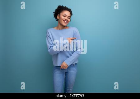 Charmante femme brune des années 20 avec boucles afro dans des vêtements décontractés élégants isolés avec fond de studio Banque D'Images