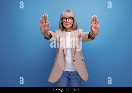 Vieille femme mature élégante dans une veste refuse quelque chose sur un fond lumineux avec un espace de copie Banque D'Images