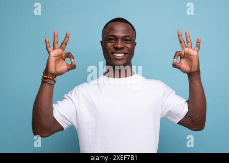 Gentil jeune africain en t-shirt blanc souriant montrant la classe avec les mains Banque D'Images