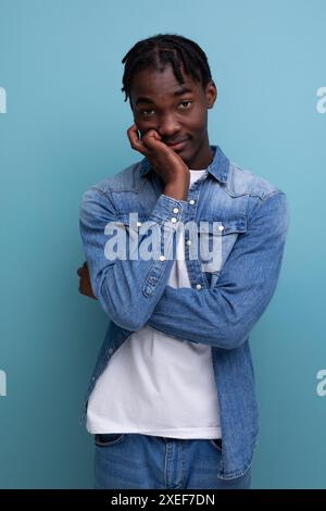 Portrait d'un jeune homme africain timide avec des dreadlocks dans une veste en denim posant soigneusement Banque D'Images