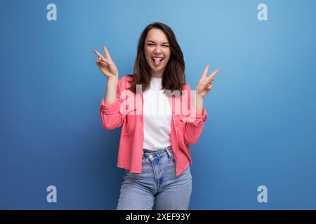 Jeune femme brune positive en chemise rose et jeans sur fond isolé de studio Banque D'Images