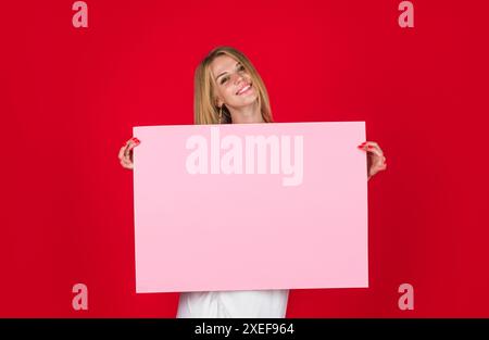 Femme souriante montrant un panneau d'affichage vierge avec un espace de copie pour le texte. Promo panneau d'enseigne de bannière. Belle fille avec affiche publicitaire vide. Publicité de Banque D'Images