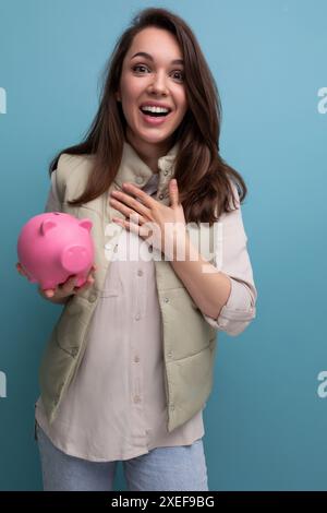 Heureuse jeune femme brune tenant de l'argent de tirelire rose Banque D'Images