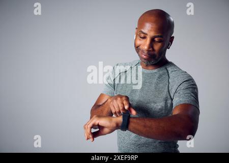 Prise de vue en studio d'un homme d'âge mûr dans des vêtements de fitness en streaming vers des écouteurs sans fil de Smart Watch Banque D'Images