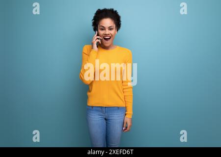 Jolie femme latine des années 20 avec cheveux afro dans une blouse jaune décontractée parlant au téléphone Banque D'Images