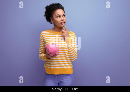 Afro brunette 20s latino jeune femme décide où investir l'argent accumulé de la banque de porc Banque D'Images