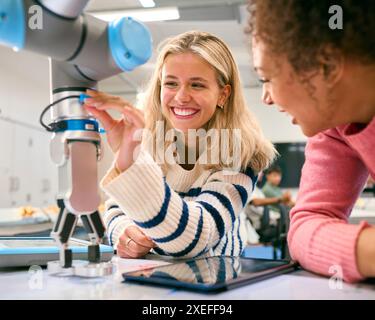 Deux étudiantes en ingénierie universitaire ou collégiale utilisant une tablette numérique pour contrôler le bras du robot Banque D'Images