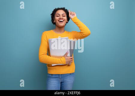 Jeune femme d'affaires hispanique réussie avec les cheveux bouclés noirs avec ordinateur portable et documents Banque D'Images