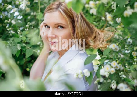 Gros plan d'un portrait d'une jeune belle femme blonde dans une chemise blanche avec des fleurs de jasmin. Atmosphère romantique et m de rêve Banque D'Images