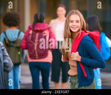 Portrait d'une étudiante du secondaire ou du secondaire à l'extérieur du bâtiment de l'école avec des enseignants et des élèves Banque D'Images