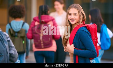 Portrait d'une étudiante du secondaire ou du secondaire à l'extérieur du bâtiment de l'école avec des enseignants et des élèves Banque D'Images