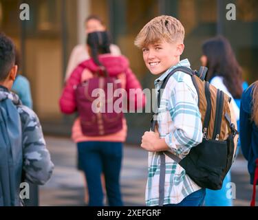 Portrait d'un étudiant masculin du secondaire ou du secondaire à l'extérieur du bâtiment scolaire avec des enseignants et des élèves Banque D'Images