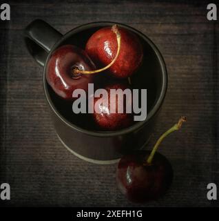 Cerises fraîches dans une tasse noire gros plan avec superposition de texture Banque D'Images