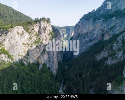 Vue aérienne d'une étroite route de montagne serpentant à travers une gorge profonde avec des falaises abruptes par une journée ensoleillée Banque D'Images