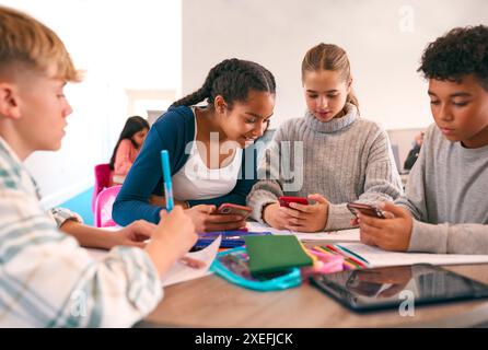 Élèves du secondaire ou du secondaire dans la zone d'étude travaillant ensemble à l'aide de téléphones portables Banque D'Images