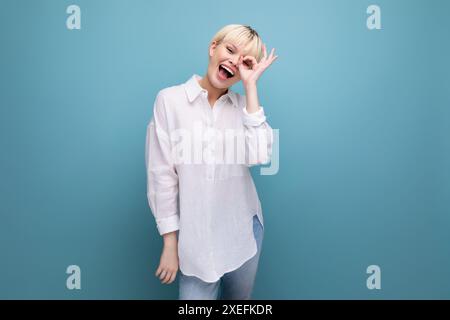Jeune femme belle ouvrière de bureau blonde avec coiffure bob et habillée en chemise blanche isolée sur fond bleu Banque D'Images