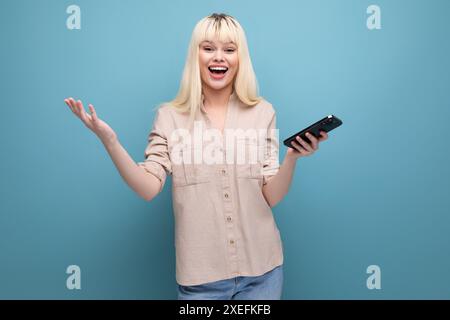 Portrait de jolie blonde satisfaite jeune femme européenne regardant l'écran du smartphone Banque D'Images